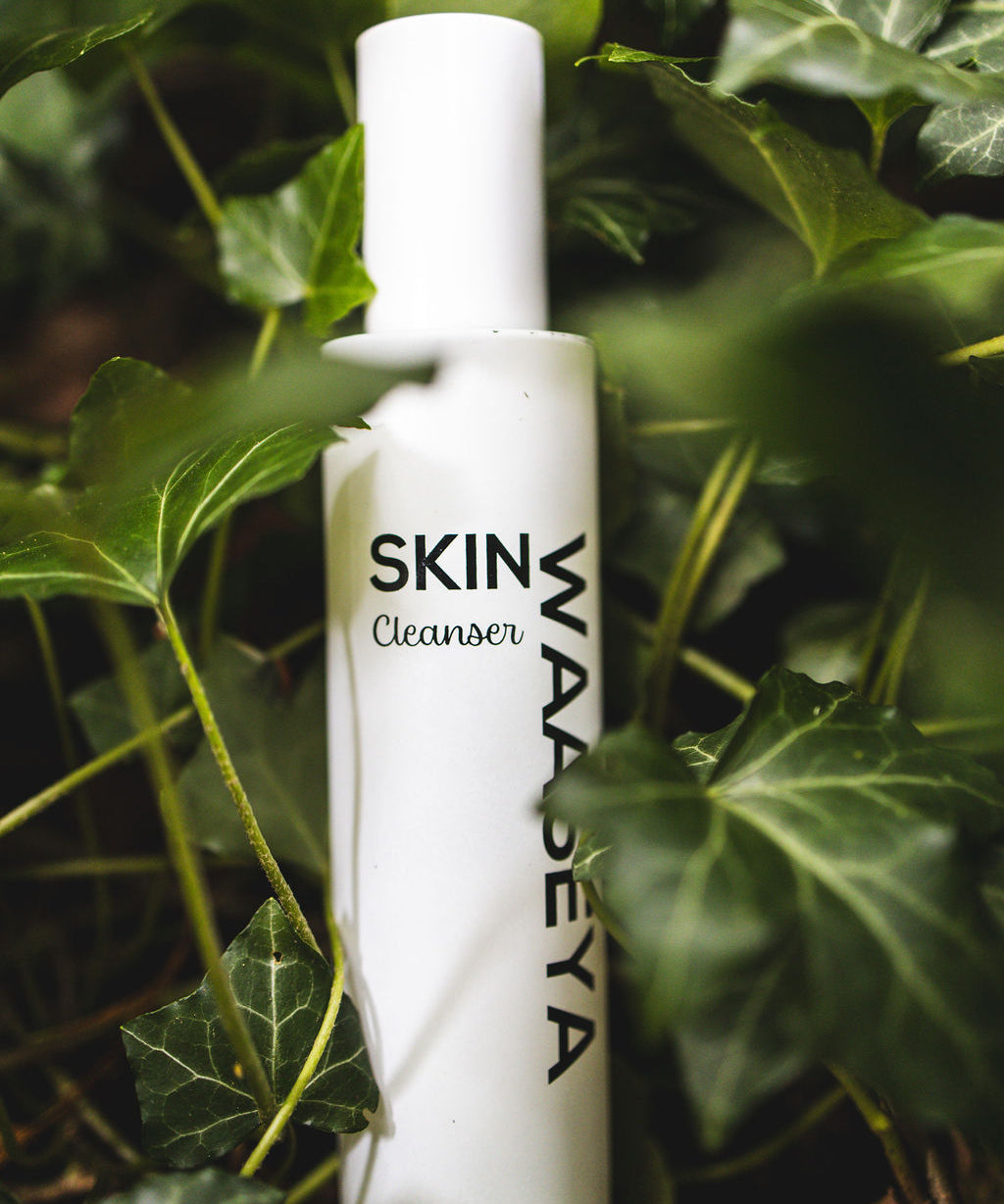 White bottle of SKIN WAASEYA Cleanser surrounded by green leaves