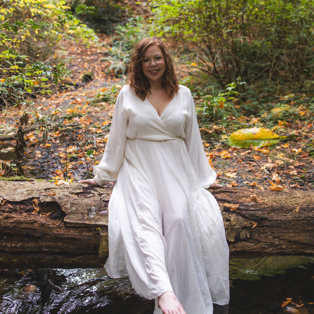 Taylor, WAASEYA founder in a white dress standing on a log over a stream in a forest